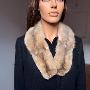 May include: A vintage black coat with a light brown fur collar. The fur collar is a light brown color and is draped around the neck of the coat. The coat has a classic design with a button closure.