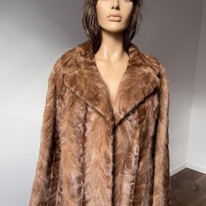 Pu&ograve; includere: Un cappotto di pelliccia marrone con colletto classico e chiusura con bottoni. Il cappotto &egrave; esposto su un manichino. La pelliccia appare morbida e ha un tono caldo e ricco. Il cappotto &egrave; in stile vintage.