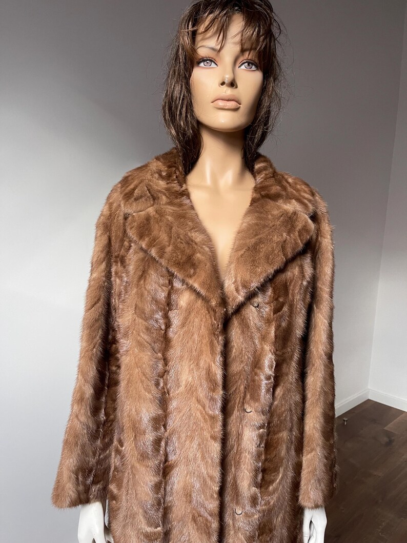 Pu&ograve; includere: Un cappotto di pelliccia marrone con colletto classico e chiusura con bottoni. Il cappotto &egrave; esposto su un manichino. La pelliccia appare morbida e ha un tono caldo e ricco. Il cappotto &egrave; in stile vintage.