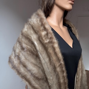 Pode incluir: Uma luxuosa estola de pele castanha com um chap&eacute;u a condizer. A estola &eacute; drapeada sobre um vestido preto, mostrando a textura macia e as ricas varia&ccedil;&otilde;es de cor da pele. O chap&eacute;u completa o elegante conjunto.