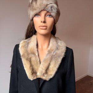 May include: A vintage fur hat and collar set. The hat is a light brown color with a rounded shape. The collar is a matching light brown fur, worn over a black coat. The mannequin is wearing the hat and collar.