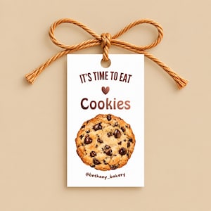 May include: A rectangular white gift tag with a brown string tied in a bow at the top. The tag features the brown text IT'S TIME TO EAT, a small brown heart, the word Cookies, a chocolate chip cookie illustration, and @bethany_bakery.