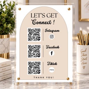 Könnte beinhalten: Ein transparenter Acryl-Schildhalter mit einem weißen und beigen bogenförmigen Einsatz mit dem Text LET'S GET Connect !, Intagram, Facebook und Tiktok. Er enthält drei schwarz-weiße QR-Codes, Social-Media-Symbole und den Text THANK YOU! unten.