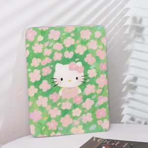 Könnte beinhalten: Eine rechteckige Tablet-Hülle mit einem leuchtend grünen Hintergrund, der mit kleinen, hellrosa Blumen bedeckt ist. In der Mitte befindet sich eine Grafik der weißen Hello Kitty-Figur mit einer rosa Schleife und einem hellrosa Kleid.