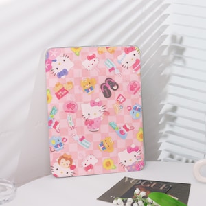 Könnte beinhalten: Rosa Tablet-Hülle mit einem sich wiederholenden Muster von Hello Kitty-Charakteren und japanischen Symbolen. Die Hülle hat einen karierten Hintergrund und einen transparenten Rand. Das Design umfasst Hello Kitty in verschiedenen Posen, Schleifen und andere dekorative Elemente.