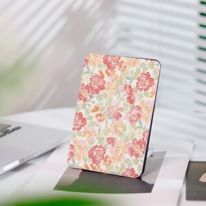Könnte beinhalten: Eine rechteckige Hülle mit floralem Muster. Das Design zeigt rote, rosa und orangefarbene Blumen und grüne Blätter auf cremefarbenem Hintergrund. Die Hülle hat einen schwarzen Rand und liegt auf einer weißen Oberfläche.