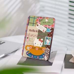 Op de afbeelding: Een kleurrijke Hello Kitty telefoonhoes met een patchwork ontwerp. De hoes heeft een cartoon afbeelding van Hello Kitty die een kopje thee vasthoudt. De tekst "Hello Kitty" is op de hoes gedrukt.