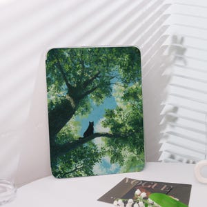 May include: A tablet case featuring a serene illustration of a black cat perched on a tree branch, set against a backdrop of lush green foliage and a blue sky. The artwork evokes a sense of tranquility and nature.