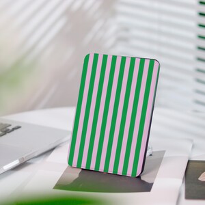 Könnte beinhalten: Eine rechteckige Handyhülle mit einem vertikalen Streifenmuster in Grün und Rosa. Die Hülle steht auf einer weißen Oberfläche, mit einem Laptop und anderen Objekten im Hintergrund. Die Hülle hat abgerundete Ecken.