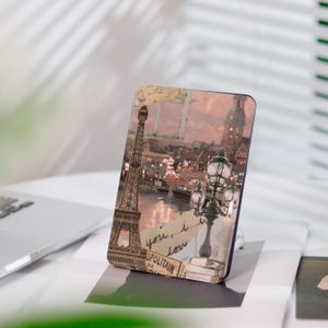 Può includere: Custodia per telefono rettangolare con una scena parigina vintage, raffigurante la Torre Eiffel, lampioni e un fiume. La custodia ha un design a collage con toni seppia e accenti di scrittura a mano.