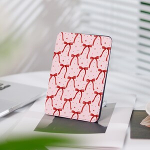 Könnte beinhalten: Eine rosa und rote E-Reader-Hülle mit einem Muster aus roten Schleifen und weißen Sternen.