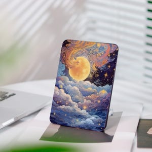 Könnte beinhalten: Eine rechteckige Handyhülle mit einem Himmelsdesign. Das Kunstwerk zeigt einen großen, goldenen Mond, der von wirbelnden Wolken in Blau-, Lila- und Orangetönen umgeben ist, mit verstreuten Sternen. Die Hülle liegt auf einer weißen Oberfläche.