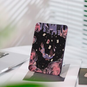 Può includere: Una custodia rettangolare per telefono con un'illustrazione surreale. Il design raffigura una persona che cade attraverso un cielo stellato, con edifici e carte fluttuanti. La tavolozza dei colori include sfumature di viola, rosa e nero.