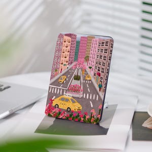 Peut inclure: Une illustration colorée d'une scène de rue de ville avec des bâtiments, un taxi jaune et des fleurs roses. Le texte "NEW YORK TAXI" est sur le côté du taxi.