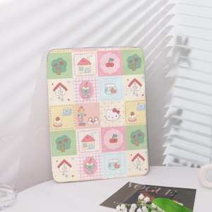 May include: A pink and green phone case with a patchwork design featuring a cartoon cat, houses, cherries, and other cute details.