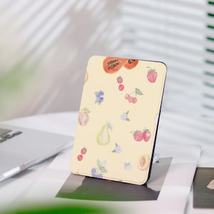 Könnte beinhalten: Eine rechteckige, hellgelbe Hülle mit schwarzem Rand, verziert mit einem Aquarell-Fruchtmuster. Das Design umfasst Papaya, Erdbeeren, Kirschen, Blaubeeren, Birnen und Pfirsiche. Die Hülle ist wahrscheinlich für ein Tablet oder einen E-Reader.