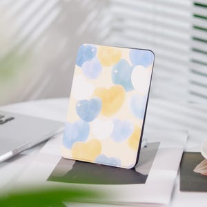 Könnte beinhalten: Eine hellgelbe und blaue Musterhülle für einen E-Reader. Die Hülle hat ein Aquarelldesign mit Herzen.