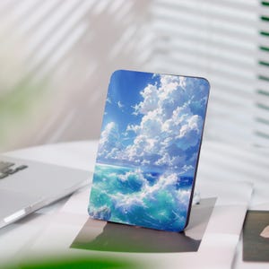 Könnte beinhalten: Eine rechteckige Handyhülle mit einer lebendigen Ozeanszene mit türkisfarbenen Wellen, weißen Schaumkronen und einem strahlend blauen Himmel voller flauschiger weißer Wolken. Die Hülle steht auf einer weißen Oberfläche.