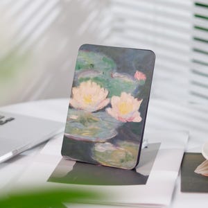 Könnte beinhalten: Eine Nahaufnahme eines Gemäldes, das zwei weiße Seerosen mit rosa Akzenten zeigt, die auf einem Teich mit grünen Seerosenblättern schwimmen. Der Hintergrund ist in sanftem Blau und Grün gehalten.