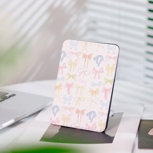 Könnte beinhalten: Eine rechteckige Hülle mit schwarzem Rand und hellrosa Hintergrund. Die Hülle ist mit einem Muster aus Aquarellschleifen in Pastellfarben bedeckt, darunter Rosa, Blau, Gelb und Grün. Die Hülle steht auf einer weißen Oberfläche.