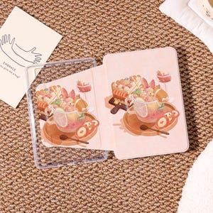 May include: A clear tablet case and a pink tablet cover with a whimsical illustration of a dessert scene. The design features a teacup, cake, and peaches. A card with the text "EMBRACE, you give me a hug?" is also visible.