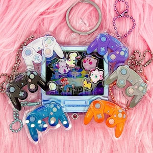 Puede incluir: Un conjunto de nueve amuletos de mando de Nintendo 64 de colores que representan a varios personajes de la franquicia de videojuegos. Los amuletos están hechos de plástico transparente y tienen un acabado holográfico.