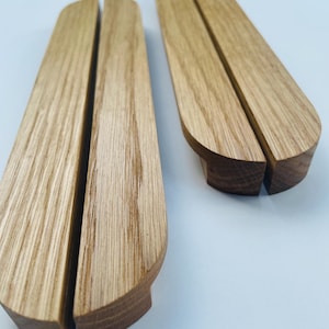 Può includere: Due supporti per telefono in legno con finitura a venature naturali. Ogni supporto ha una parte superiore curva e una fessura per tenere un telefono. I supporti sono realizzati in legno chiaro e sono progettati per un tavolo o una scrivania.