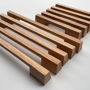 Può includere: Una collezione di maniglie per mobili in legno, con venatura naturale. Le maniglie sono rettangolari con maniglia e base, ideali per cassetti o armadi. Il colore marrone caldo e il design semplice suggeriscono un'estetica moderna.