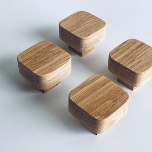 Op de afbeelding: Vier vierkante houten kastknoppen met afgeronde hoeken zijn gerangschikt op een wit oppervlak. De knoppen zijn gemaakt van lichtgekleurd hout, dat de natuurlijke nerfstructuur laat zien. Elke knop is ongeveer 4 cm breed.