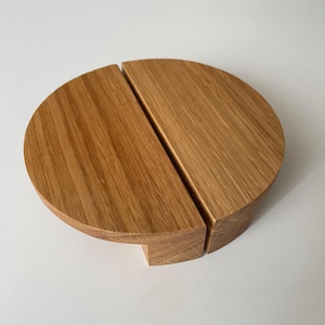 Pode incluir: Objeto de madeira clara, semicircular, dividido em duas partes. O veio da madeira é visível. Poderia ser um elemento decorativo ou funcional, como uma pega ou parte de um objeto maior.