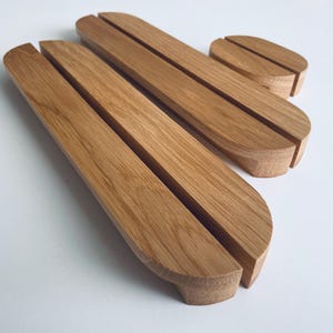 Op de afbeelding: Een set van vier houten naambordhouders. De houders zijn gemaakt van lichtbruin hout en hebben een gebogen ontwerp met een sleuf voor het vasthouden van kaarten. De set bevat twee grotere houders en twee kleinere.