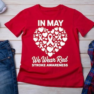 Peut inclure: T-shirt rouge avec un motif de cœur blanc. Le cœur est rempli de rubans blancs et de cœurs. Le texte "IN MAY We Wear Red STROKE AWARENESS" est imprimé sous le cœur.