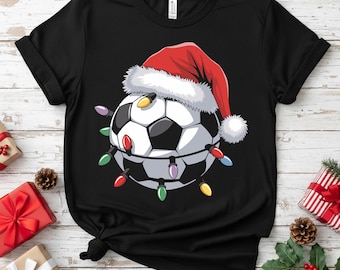 May include: Black t-shirt featuring a soccer ball wearing a Santa hat and wrapped in colorful Christmas lights. The soccer ball has black and white panels. A festive holiday design for soccer fans.