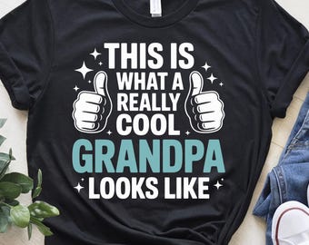 May include: Black t-shirt with white text that reads "This is what a really cool Grandpa looks like."  Two white thumbs up are on either side of the text.  There are small white stars around the text.