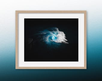 May include: A framed photograph of a large wave breaking in the ocean. The wave is white and blue, and the water is dark blue. The photograph is framed in a light wood frame.