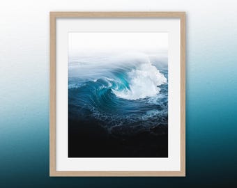 May include: A framed photograph of a large ocean wave crashing in the water. The wave is a deep blue color with white foam at the top. The background is a light blue sky.
