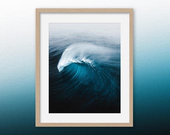 May include: A framed photograph of a large wave breaking in the ocean. The wave is a deep blue color and the water is a lighter blue. The wave is breaking in a powerful and dramatic way.