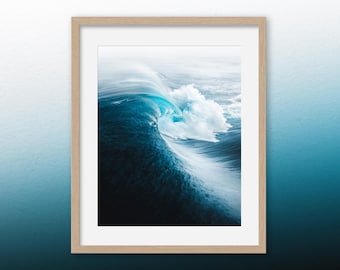 May include: A close-up photograph of a large wave breaking in the ocean. The wave is a deep blue color with white foam at the crest. The water is a deep blue color and the sky is a light blue color.