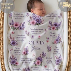 May include: A white baby blanket featuring purple and pink floral clusters and various Bible verses. The center displays the name Olivia Grace in dark purple text. The blanket is decorated with lavender sprigs and scriptural quotes.