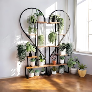 Puede incluir: Un estante para plantas en forma de corazón, hecho de metal negro y madera, lleno de varias plantas en macetas. El estante tiene múltiples estantes y cestas colgantes, creando una exhibición de jardín vertical. Las plantas incluyen helechos, suculentas y otras plantas verdes.