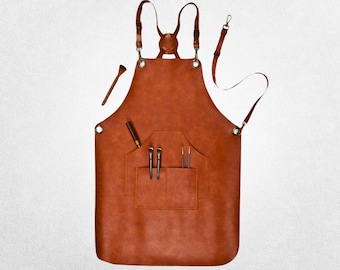 Puede incluir: Un delantal de cuero marrón con correas ajustables y un bolsillo grande. El bolsillo tiene múltiples ranuras para herramientas para guardar pinceles, bolígrafos u otras herramientas.
