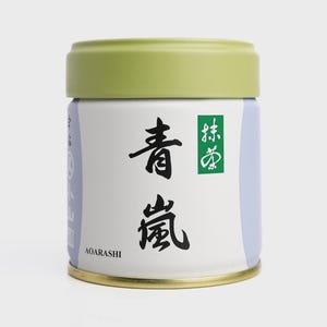 May include: A round tin of matcha green tea with a light green lid and a gold-coloured base. The white body features Japanese characters in black and a green square with more Japanese text. The brand name "AOARASHI" is printed at the bottom.