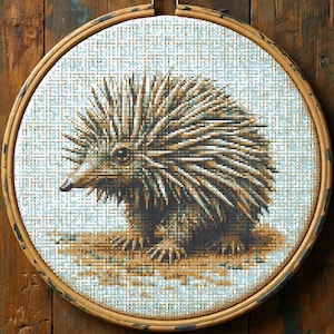 May include: A cross-stitch embroidery of an echidna, a spiky, brown and tan mammal, set in a wooden embroidery hoop. The echidna is centered against a light blue and white background, with detailed stitching creating texture and depth.