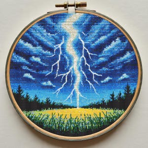 May include: A cross-stitch embroidery of a lightning bolt striking a field. The artwork is set in a round wooden hoop. The sky is dark blue with white and light blue clouds. The field is yellow and green, with dark green trees in the background.