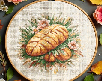 Könnte beinhalten: Kreuzstich-Stickerei in einem Holzrahmen mit einem Brotlaib und Kürbissen, umgeben von Blumen und Grün. Die Stickerei ist in Orange-, Gelb-, Grün- und Rosatönen gehalten. Der Rahmen hat einen Durchmesser von etwa 20 cm.