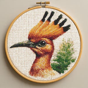 May include: A cross-stitch hoop art featuring a detailed portrait of a Hoopoe bird. The bird has orange and black plumage, a long, curved beak, and a distinctive crest. The artwork is set in a round wooden hoop.