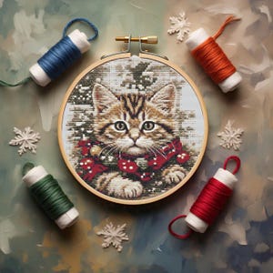 Peut inclure: Un cercle de broderie au point de croix avec un chat tigré portant une écharpe rouge, entouré de bobines de fil bleu, orange, vert et rouge. Des décorations de flocons de neige blancs sont dispersées autour du cercle sur un fond texturé.