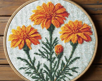 May include: A cross-stitch embroidery featuring orange marigold flowers with green stems and leaves, set against a white backdrop. The embroidery is presented in a round wooden hoop, highlighting the detailed needlework and vibrant colours.