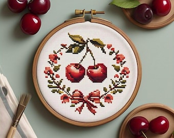 May include: A cross-stitch embroidery hoop featuring a pair of red cherries with green leaves, surrounded by a floral wreath and a red bow. The embroidery is set in a wooden hoop, with fresh cherries nearby.