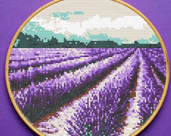 May include: A cross-stitch embroidery of a lavender field in a wooden hoop. The scene features rows of purple lavender, a green treeline, and a cloudy sky. The embroidery is set against a purple background.